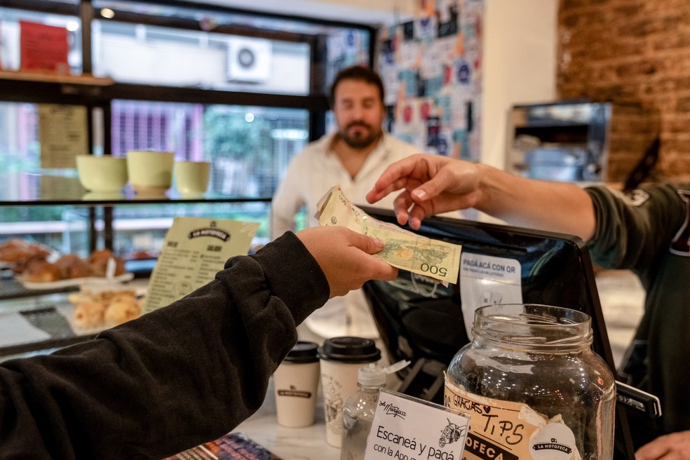 Um cliente paga com cédulas de peso argentino em um café em Buenos Aires — Foto: Erica Canepa/Bloomberg