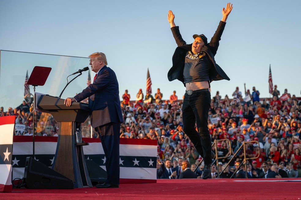 O CEO da Tesla e da SpaceX, Elon Musk, sobe ao palco e se junta a Donald Trump durante um comício de campanha no local da primeira tentativa de assassinato do ex-presidente, em Butler, Pensilvânia, em outubro — Foto: Jim WATSON / AFP