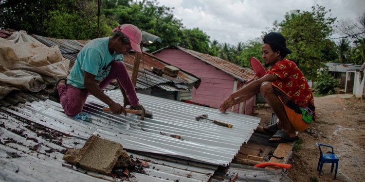 Dois homens consertam o telhado de uma casa após a passagem da tempestade tropical Melissa, antes de se tornar um furacão, em Barahona, na República Dominicana, em 28 de outubro de 2025 — Foto: AFP