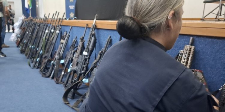 Policial mostra parte dos 91 fuzis enfileirados durante coletiva na Cidade da Polícia, no Jacaré — Foto: Marcos Nunes/Agência O GLOBO
