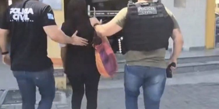 Suspeita sendo conduzida por policiais pouco antes de entrar na DHBF — Foto: Reprodução