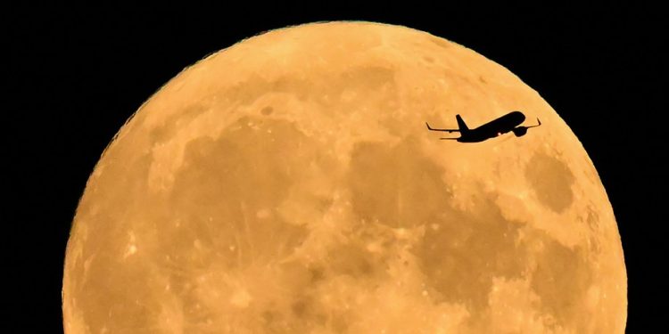 Um Airbus A320 se preparando para pousar na Inglaterra, sobrevoa a lua cheia nascendo no céu de Londres — Foto: JUSTIN TALLIS / AFP