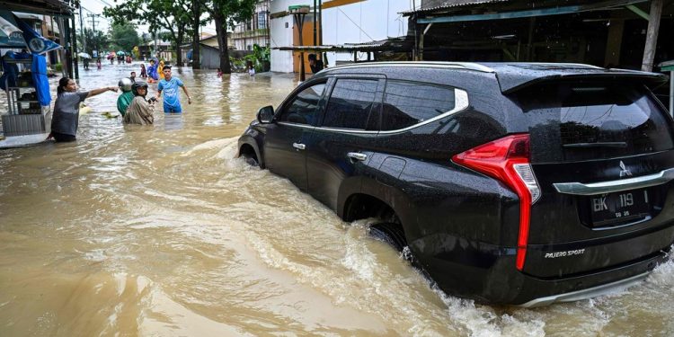 Moradores (à esquerda) pedem a um motorista que dirija devagar em meio à enchente em Medan, Sumatra do Norte — Foto: YT Hariono / AFP