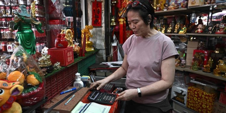 Thitinan Suntisubpoo usa calculadora em sua loja em Banckoc — Foto: Lillian Suwanrumpha/ AFP