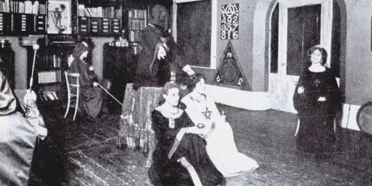 Encapuzado, Crowley está atrás dos fieis durante um rito de magia negra — Foto: Reprodução | La Nación