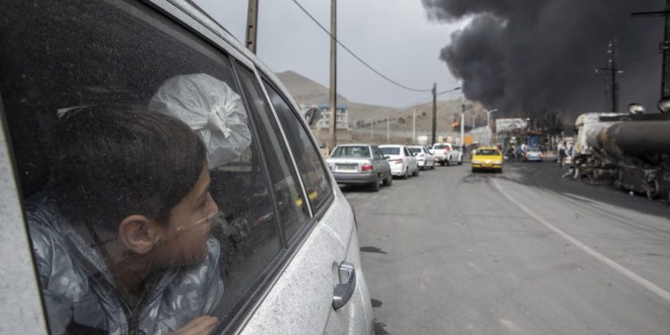 Um menino observa colunas de fumaça subindo de um depósito de petróleo em Teerã, Irã, no domingo, 8 de março de 2026, após ataques noturnos das forças americanas e israelenses — Foto: Arash Khamooshi / New York Times