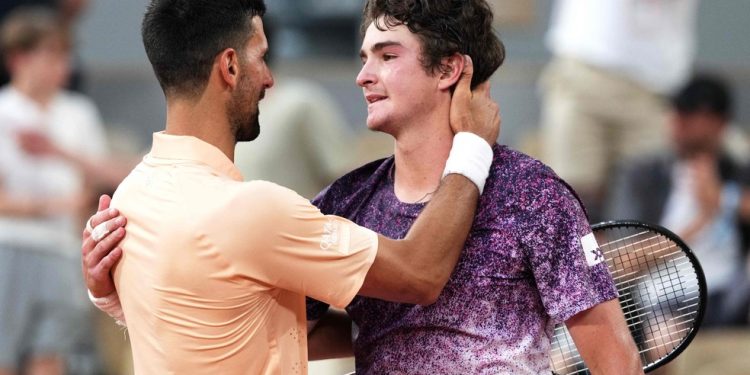 O brasileiro João Fonseca (à direita), cumprimenta o sérvio Novak Djokovic ao final da partida de simples masculina do sexto dia do torneio de tênis do Aberto da França, na quadra Philippe-Chatrier, no complexo de Roland-Garros — Foto: Dimitar DILKOFF / AFP