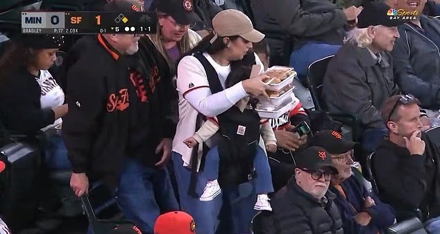 Torcedor de beisebol é criticado nas redes após companheira ser flagrada carregando bebê e comida enquanto ele permanece sentado; assista